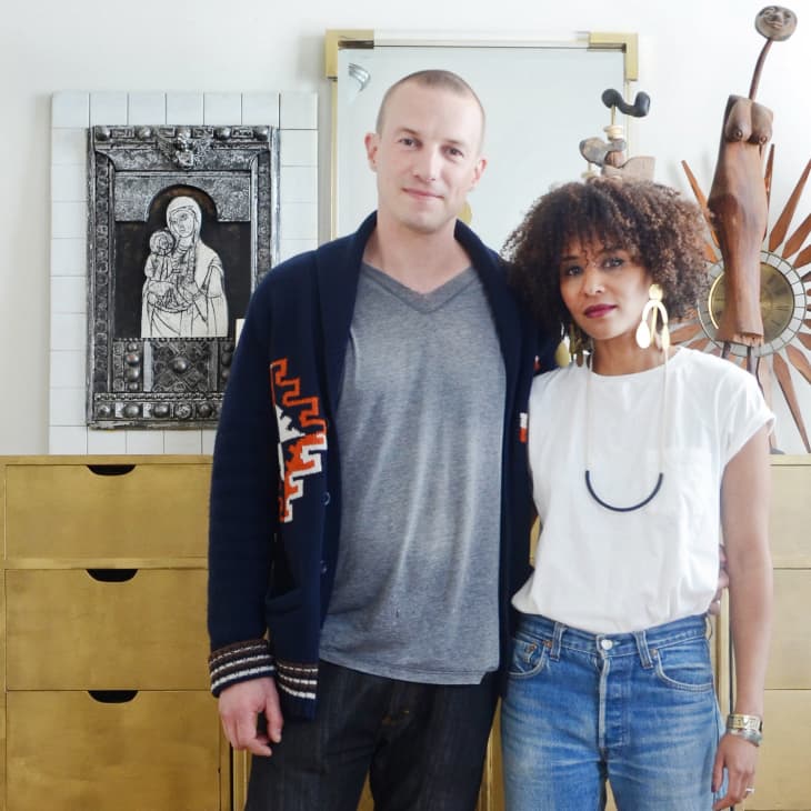 Two people standing in front of a gold dresser with art pieces and sculptures in a modern room.