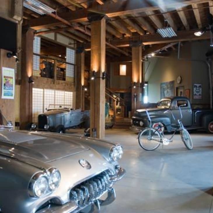 Classic cars and a bicycle in a rustic garage with wooden beams and vintage posters.