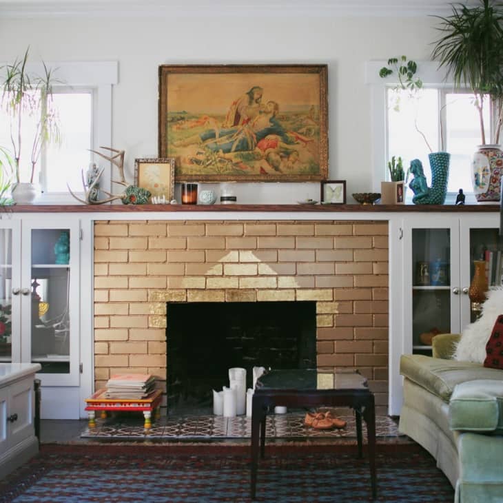 Living room with a brick fireplace, green sofa, plants, and a painting above the mantel.