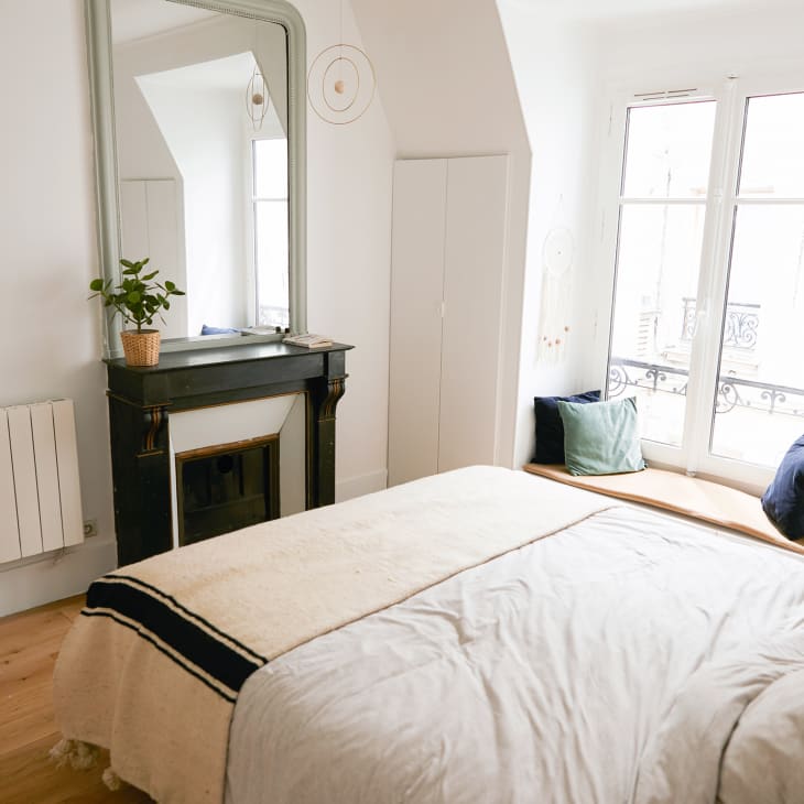Cozy bedroom with a fireplace, large mirror, potted plant, and window seat with cushions.