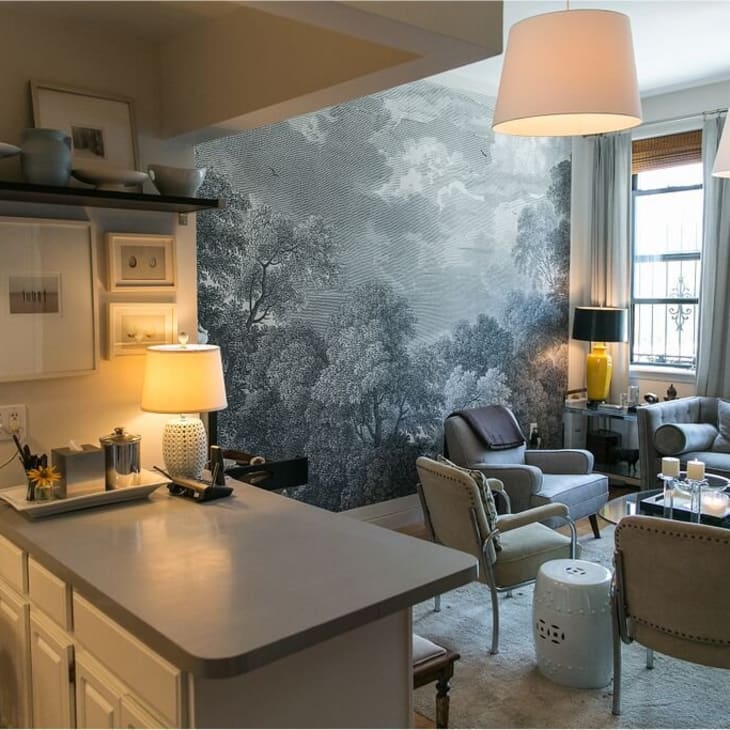 Cozy living room with gray sofa, armchairs, landscape mural, and soft lighting from table lamps.