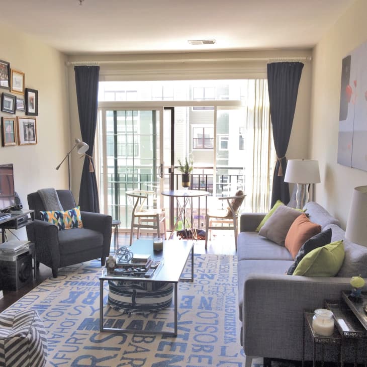 Living room with gray sofa, colorful cushions, gallery wall, TV, and a small dining table by large windows with dark curtains.