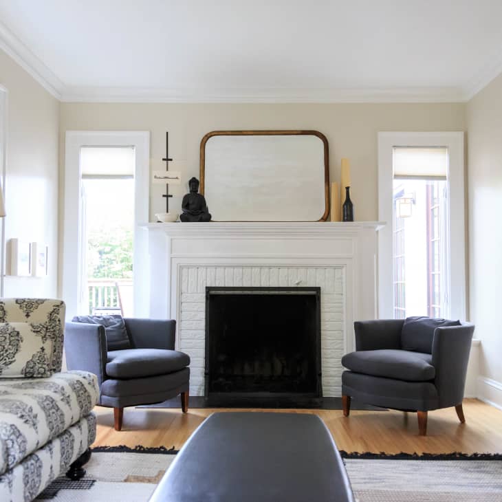 Living room with white fireplace, two gray chairs, patterned sofa, and a large mirror above the mantel.