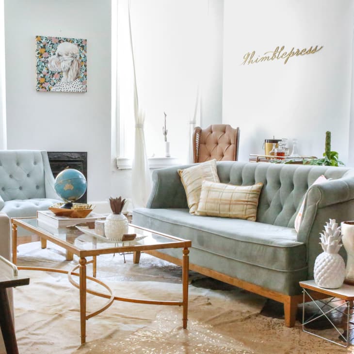 Living room with tufted sofas, glass coffee table, globe, and decorative plants. Wall art and "Whimblepress" sign visible.