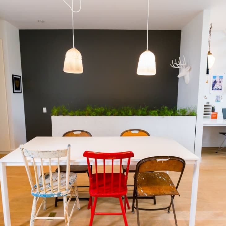 Dining area with mismatched chairs, white table, pendant lights, and a wall planter. Desk and stairs in the background.