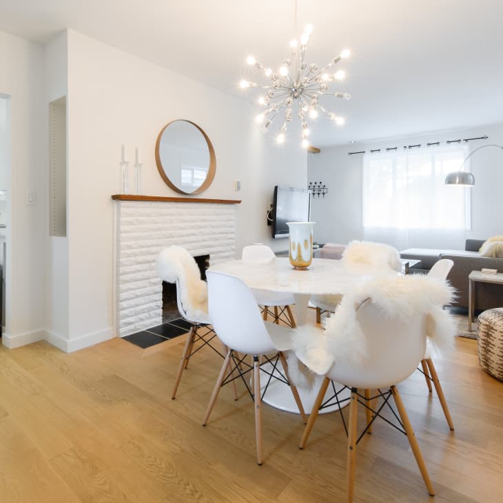 Open-plan living and dining area with white chairs, round table, modern chandelier, and a cozy gray sofa.