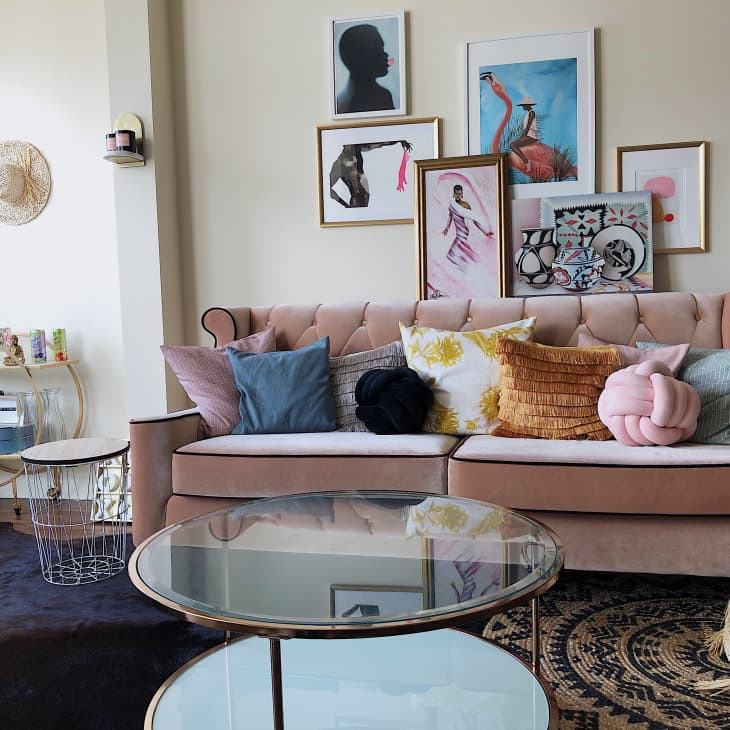 Beige sofa with colorful pillows, gallery wall art, round glass tables, and a gold bar cart in a stylish living room.