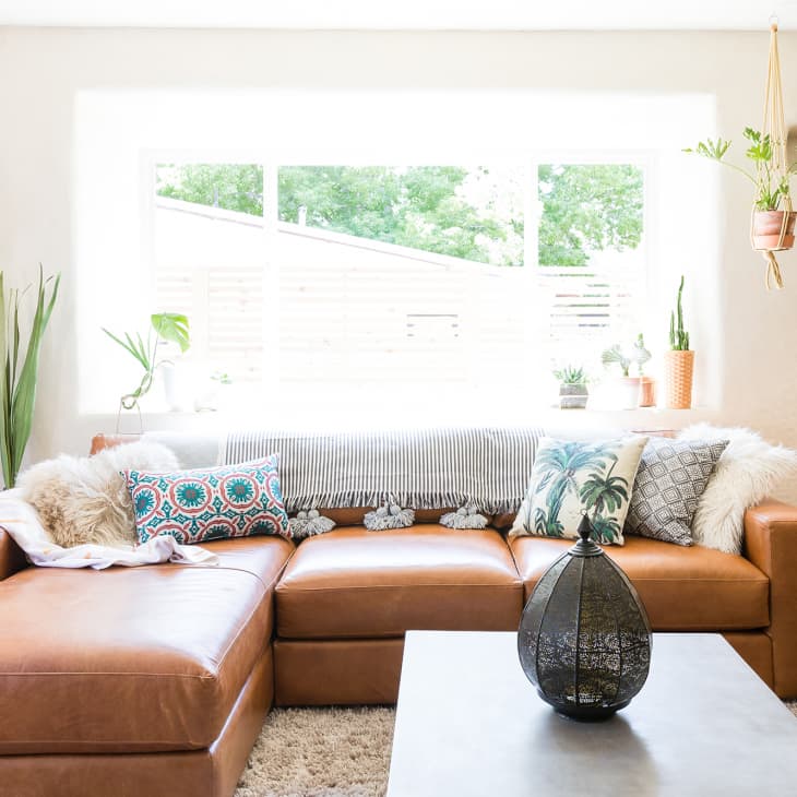 Brown leather sectional sofa with patterned pillows, plants, and a modern coffee table in a bright living room.