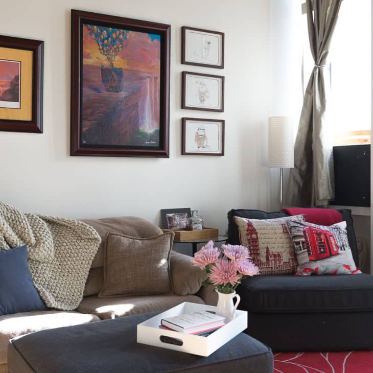 Cozy living room with framed art, gray sofa, red and white pillows, knit throw, and a tray with flowers on an ottoman.