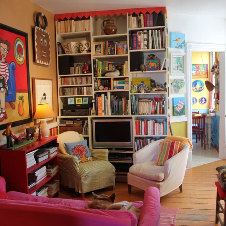 Colorful living room with eclectic decor, bookshelves, vibrant artwork, and cozy seating, leading to a bright dining area.