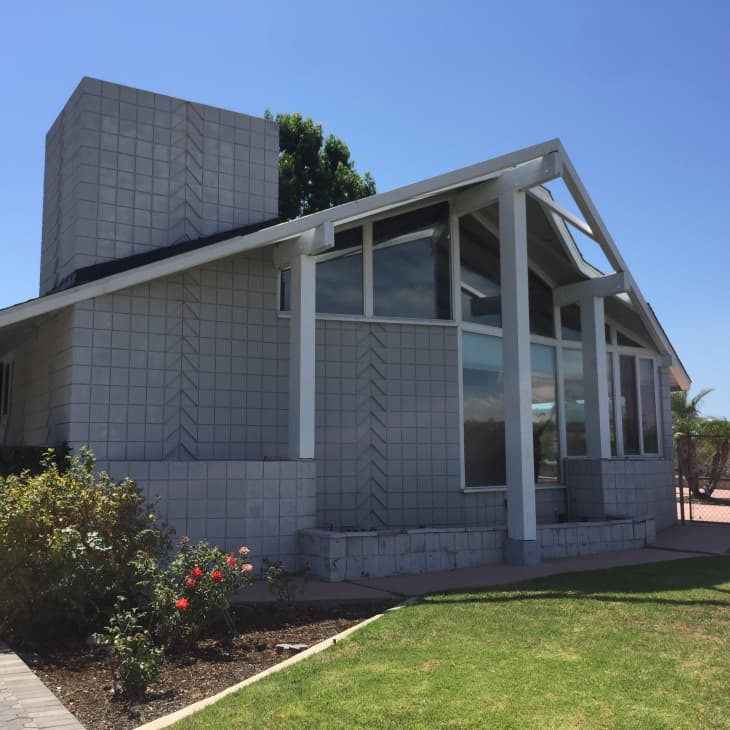 Modern house with large windows, geometric facade, and a garden with rose bushes under a clear blue sky.