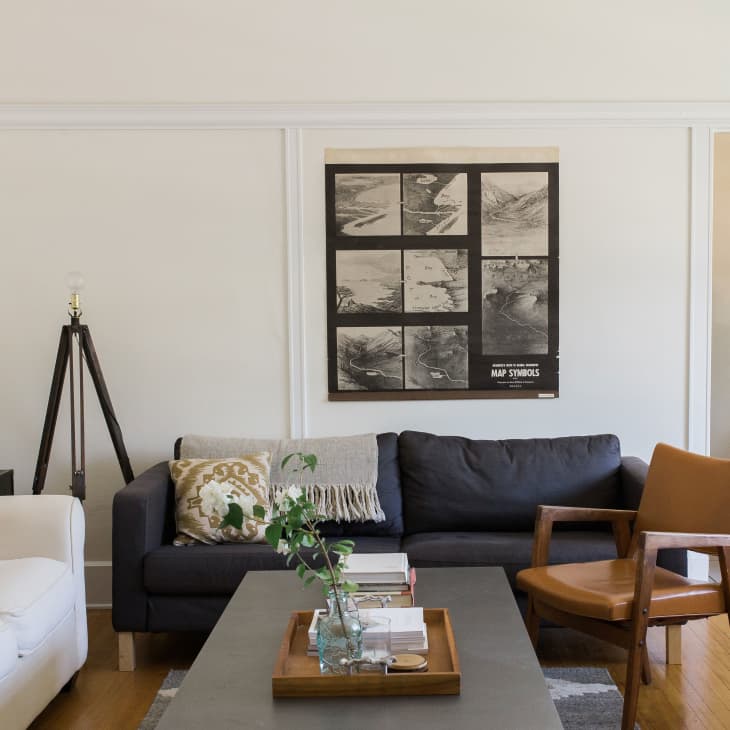 Living room with a dark gray sofa, white armchair, wooden chair, and a wall art collage above.