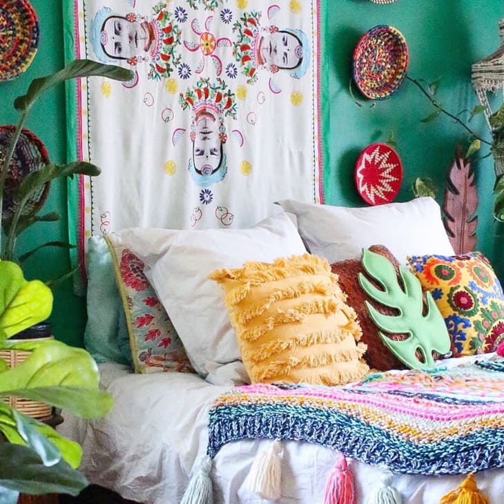 Bohemian bedroom with green walls, colorful pillows, plants, and woven wall decor.