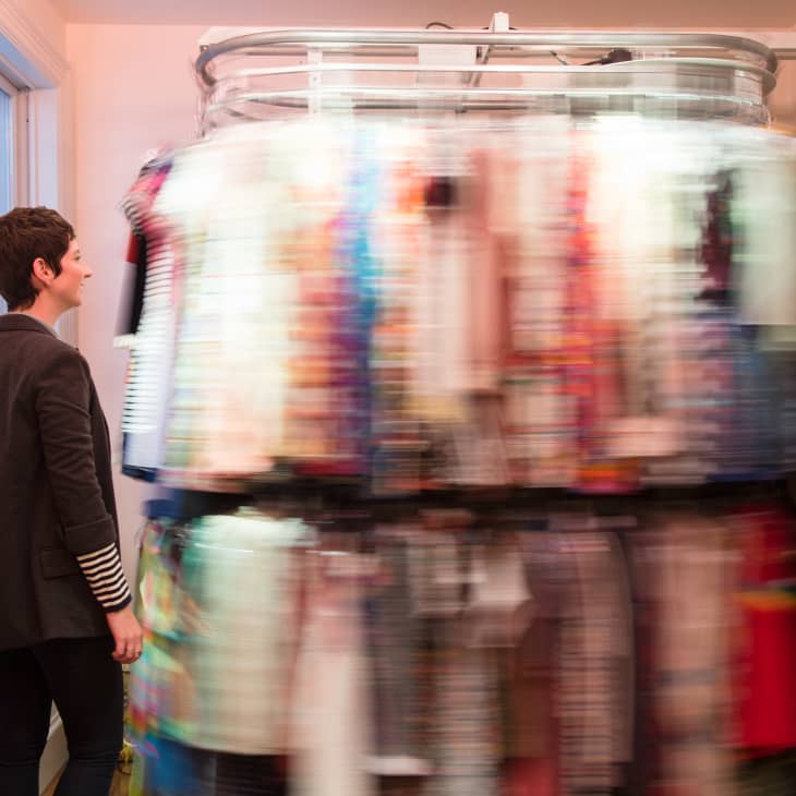 Person observing a rotating closet rack filled with colorful clothes in a small room.