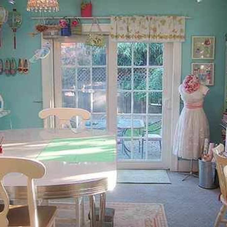 Craft room with turquoise walls, sewing mannequin, large table, and French doors leading to a garden.