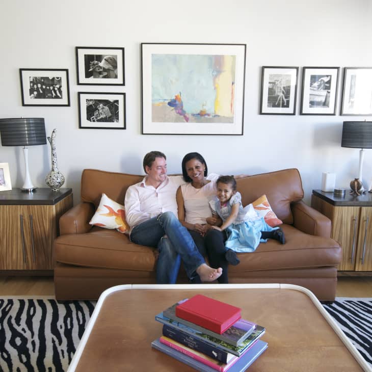 Family sitting on a brown leather sofa in a living room with framed art, zebra rug, and wooden side tables.