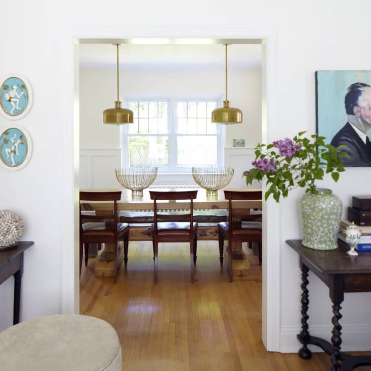 Living room with eclectic decor, leading to dining area with wooden table, chairs, and brass pendant lights.