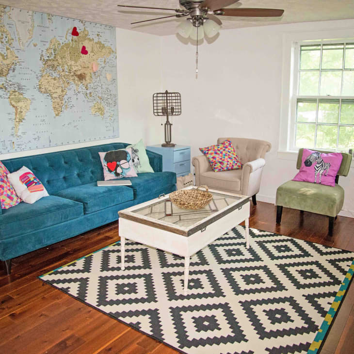 Living room with teal sofa, colorful pillows, world map wall art, geometric rug, and guitar on the wall.
