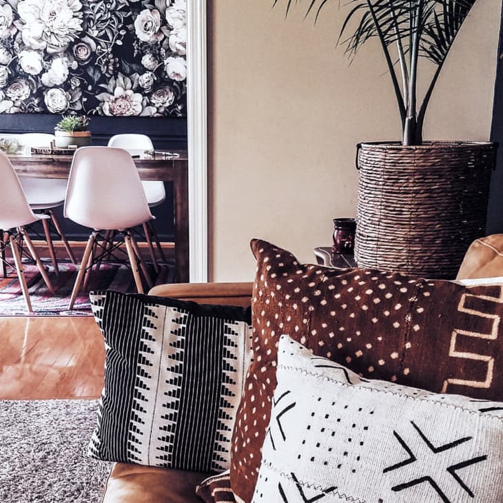 Living room with patterned cushions on a tan sofa, large potted plant, and view into dining area with white chairs and floral artwork.