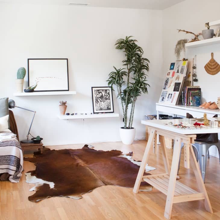 Creative studio with a daybed, cowhide rug, potted plants, and a white desk with art supplies and books.