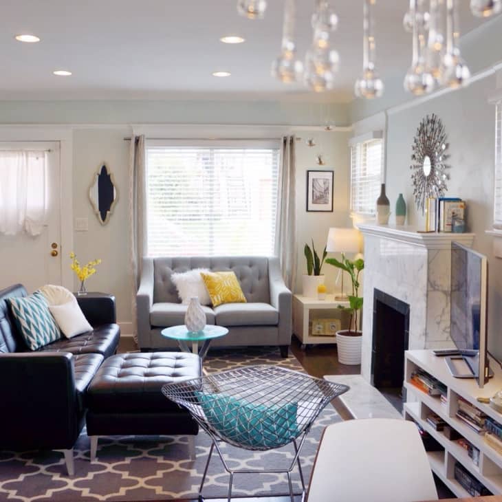 Cozy living room with black leather sofa, gray armchair, geometric rug, and decorative mirror above a white fireplace.