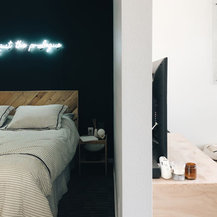 A bed under a neon light that reads "this is just the prologue"