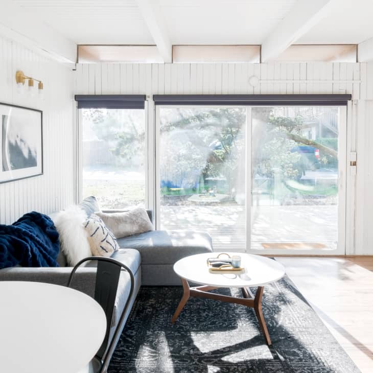 Bright living room with sliding glass doors, white walls, a gray sofa, round coffee table, and wall art.