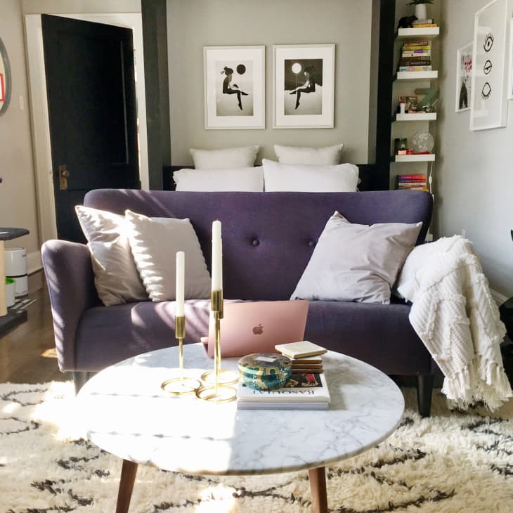 Cozy living room with a purple sofa, marble coffee table, books, candles, and wall art, featuring a cat tree and plants.