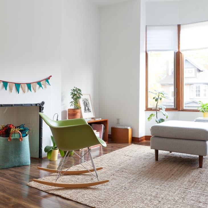 Living room with green rocking chair, gray sofa, fireplace with bunting, and large windows overlooking houses.