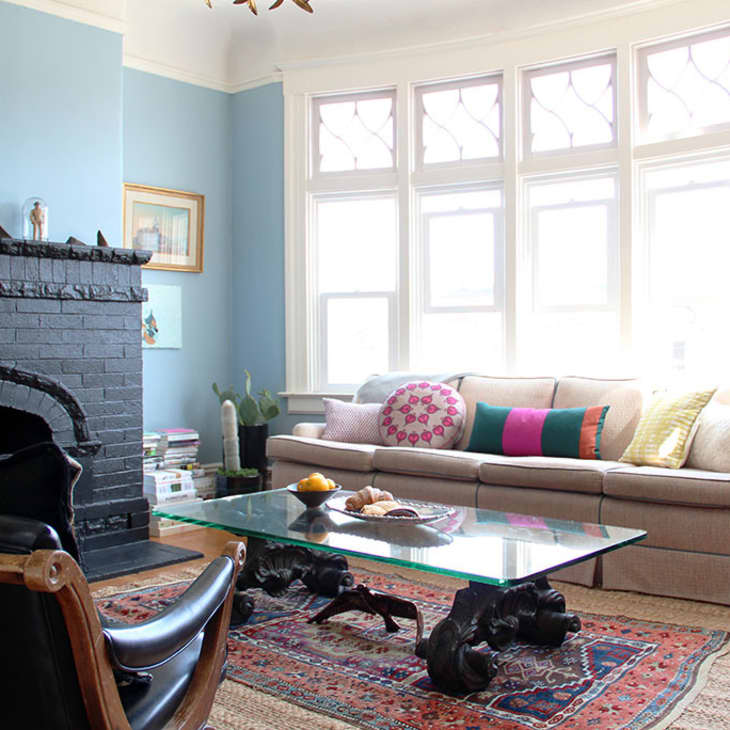 Living room with a black brick fireplace, beige sectional sofa, colorful pillows, glass coffee table, and patterned rug.