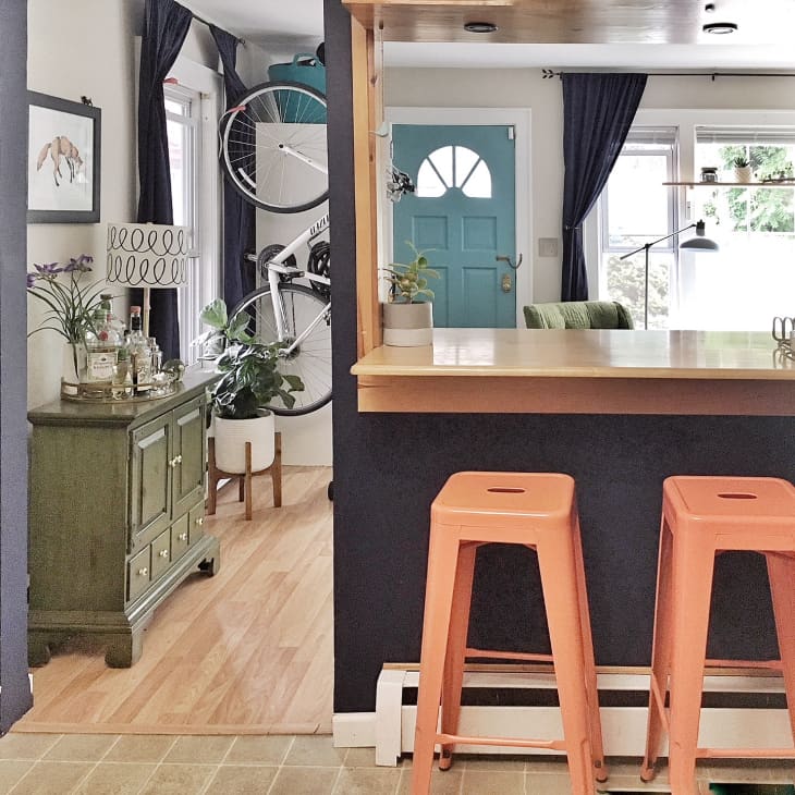 Kitchen with wooden counter, two orange stools, green sideboard, and a bicycle mounted on the wall near a blue door.