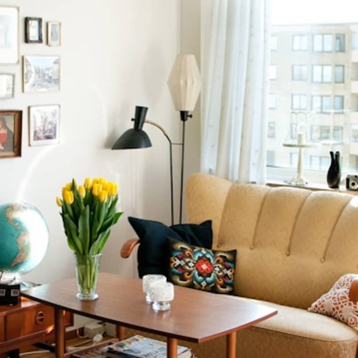 Cozy living room with a yellow armchair, globe, wall art, and a vase of yellow tulips on a wooden coffee table.