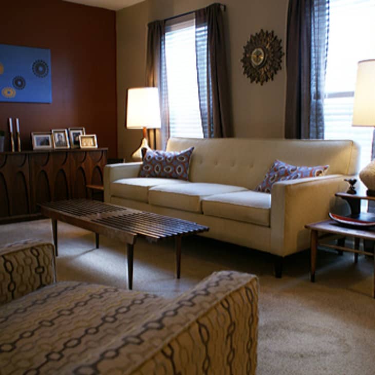 Mid-century modern living room with cream sofa, patterned armchair, wooden coffee table, and decorative wall art.
