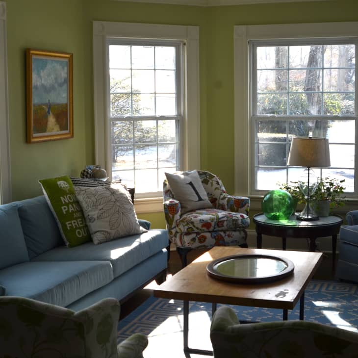 Living room with blue sofa, patterned armchairs, numbered pillows, green walls, and large windows.
