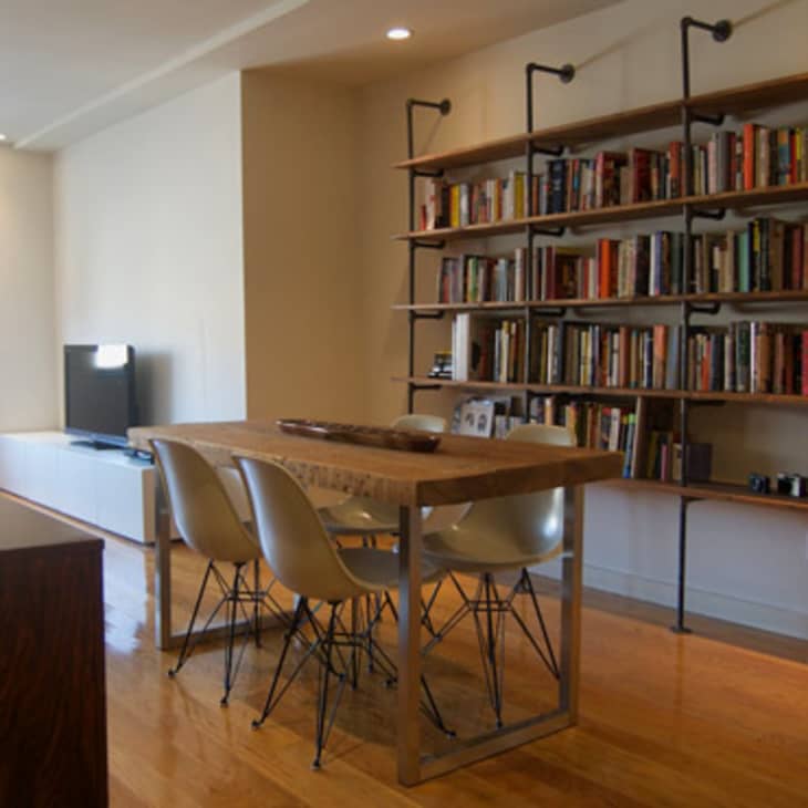 Dining area with wooden table, four white chairs, and a large bookshelf filled with books and cameras.