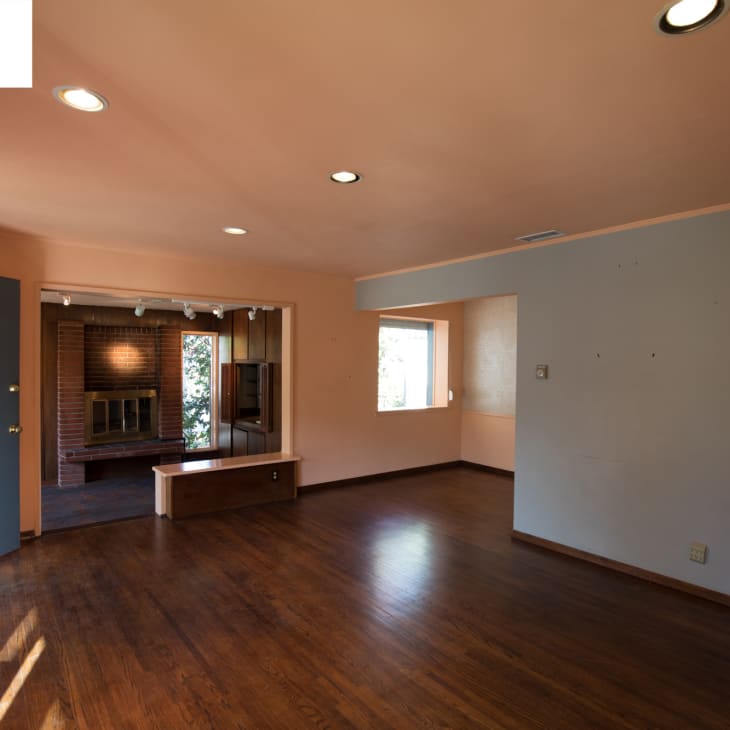Empty living room with hardwood floors, recessed lighting, and a brick fireplace in the adjacent room.