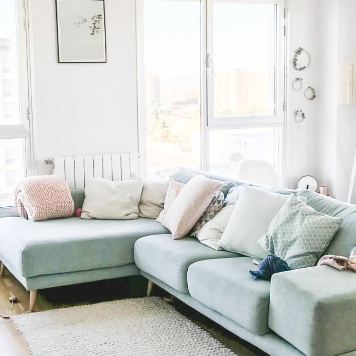Light-filled living room with a pastel blue sectional sofa, assorted cushions, and a floor lamp by large windows.