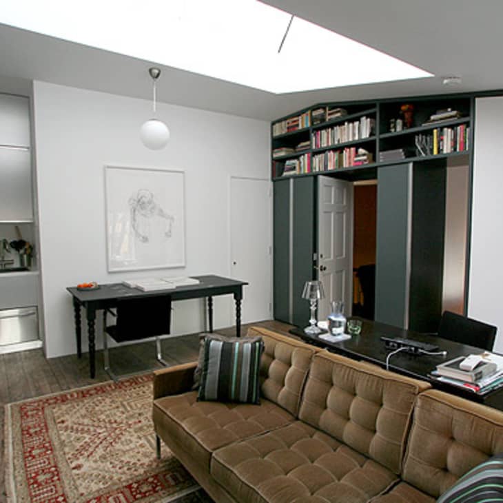Modern living room with brown sofa, striped cushions, dark wood table, built-in bookshelves, and skylight.