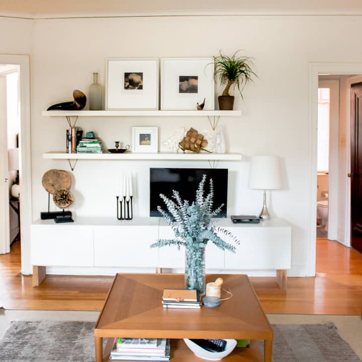 Living room with white shelves, TV, decor items, wooden coffee table, and a plant in a vase.
