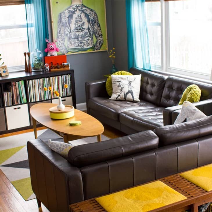 Mid-century modern living room with black leather sofas, turquoise curtains, vinyl records, and a wooden coffee table.