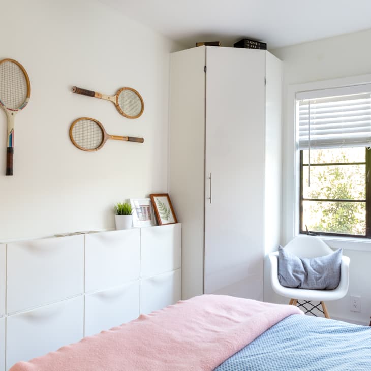 Bedroom with tennis rackets on the wall, white storage units, a chair by the window, and a bed with pink and blue bedding.