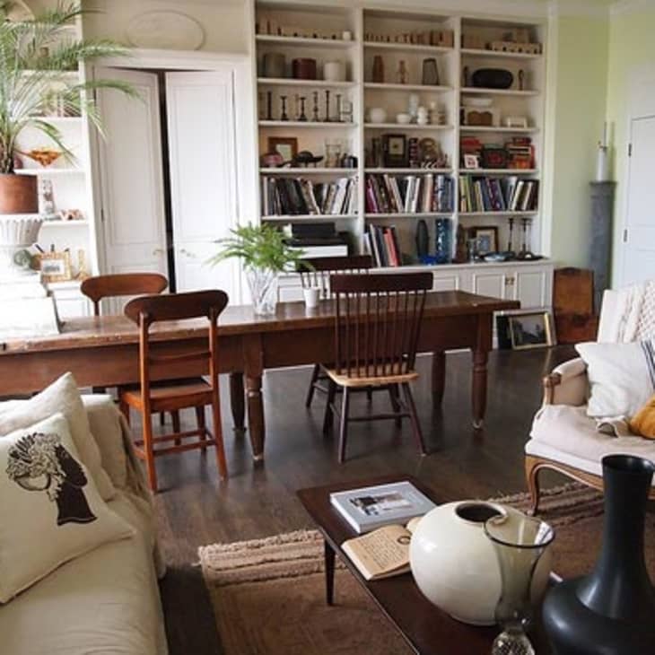 Living room with a long wooden table, assorted chairs, bookshelves, and cozy seating with decorative pillows.