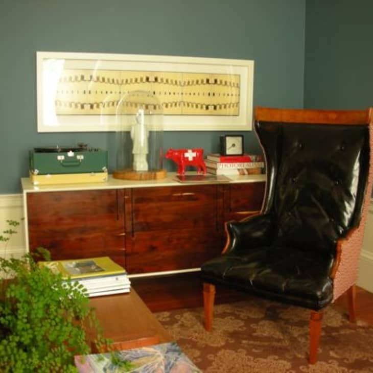 Mid-century modern room with a black leather wingback chair, wooden sideboard, and blue walls.