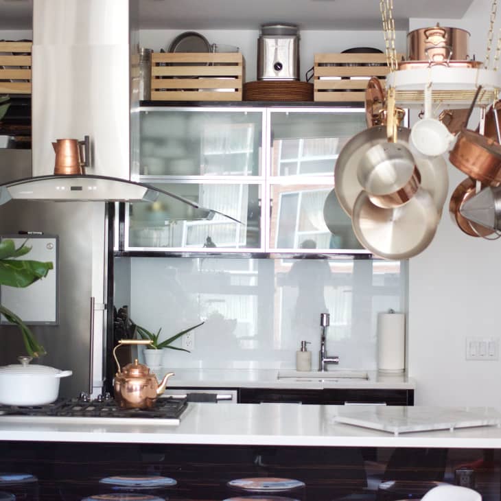 Modern kitchen with hanging copper pots, white countertop, potted plant, and stainless steel appliances.