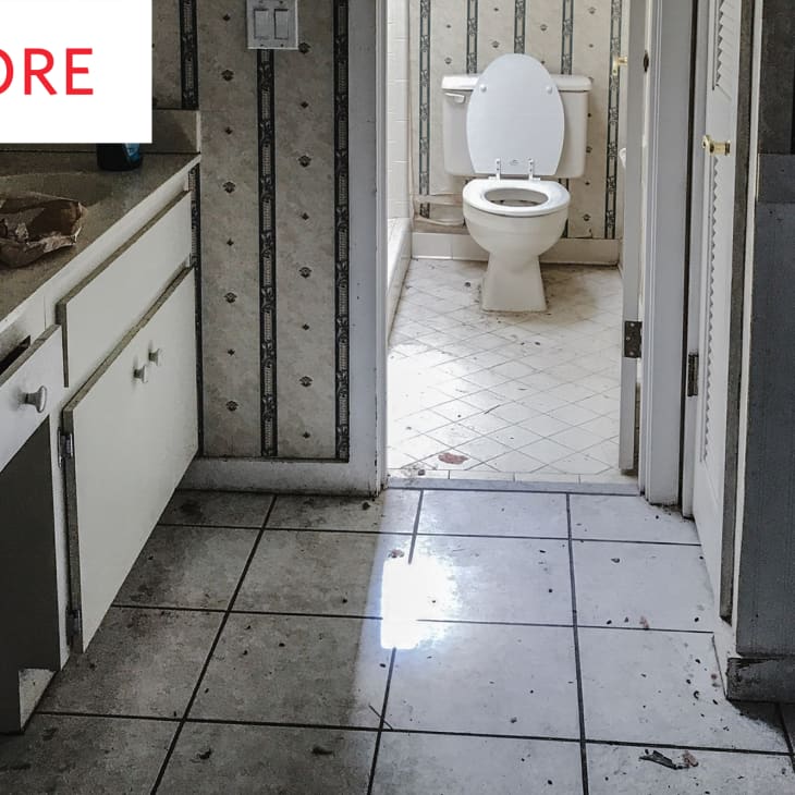 Dirty bathroom with tiled floor, white cabinets, and a toilet. Peeling wallpaper and grime visible on surfaces.