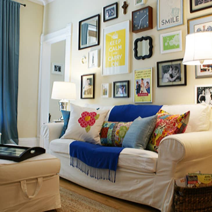 Living room with white sofa, colorful pillows, blue throw, gallery wall, and floor lamps.