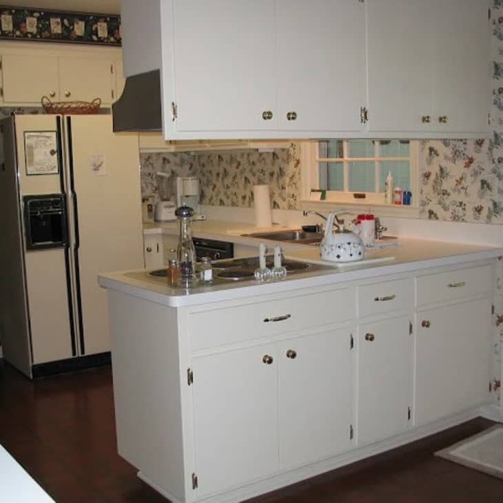White kitchen with floral wallpaper, white cabinets, stainless steel sink, and a white refrigerator.