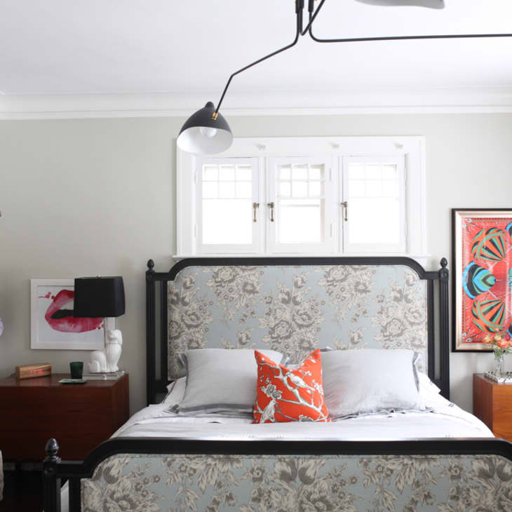 Bedroom with floral headboard, orange accent pillow, two wooden nightstands, and a shelf with handbags.