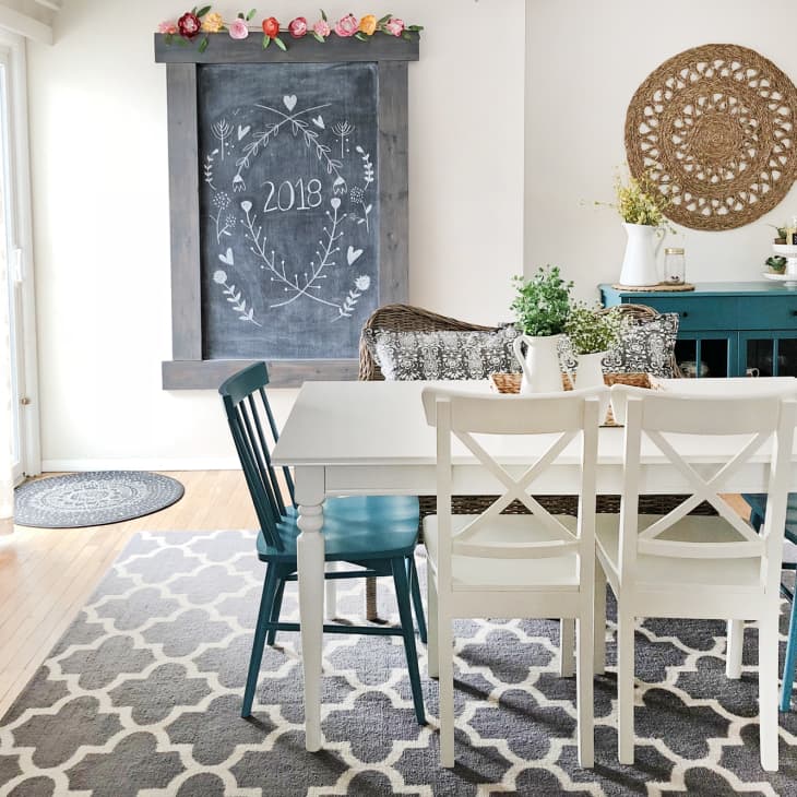 Dining room with white table, blue and white chairs, chalkboard art, and a blue sideboard with decor items.