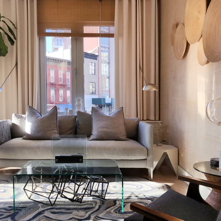 Modern living room with gray sofa, glass coffee table, abstract rug, and wall-mounted wooden decor.